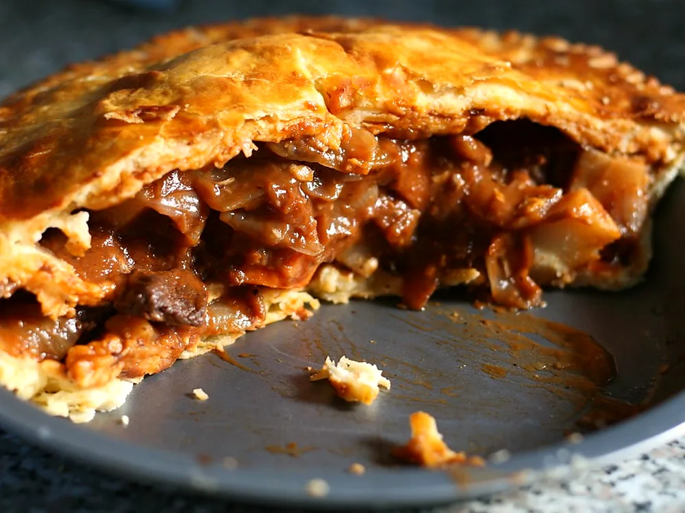 A freshly baked meat pie broken open to show the filling