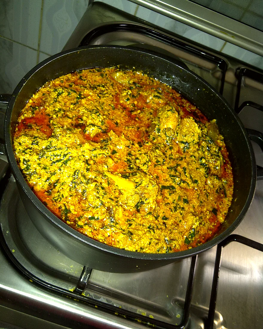 A wide pot of egusi soup simmering on a gas burner